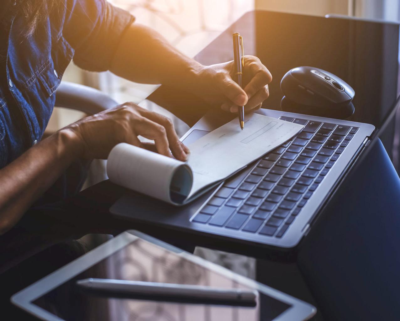 Business woman hand writing and signing white blank bank cheque book with laptop computer, mouse and digital tablet on the desk at office. Payment by check, paycheck, payroll concept.