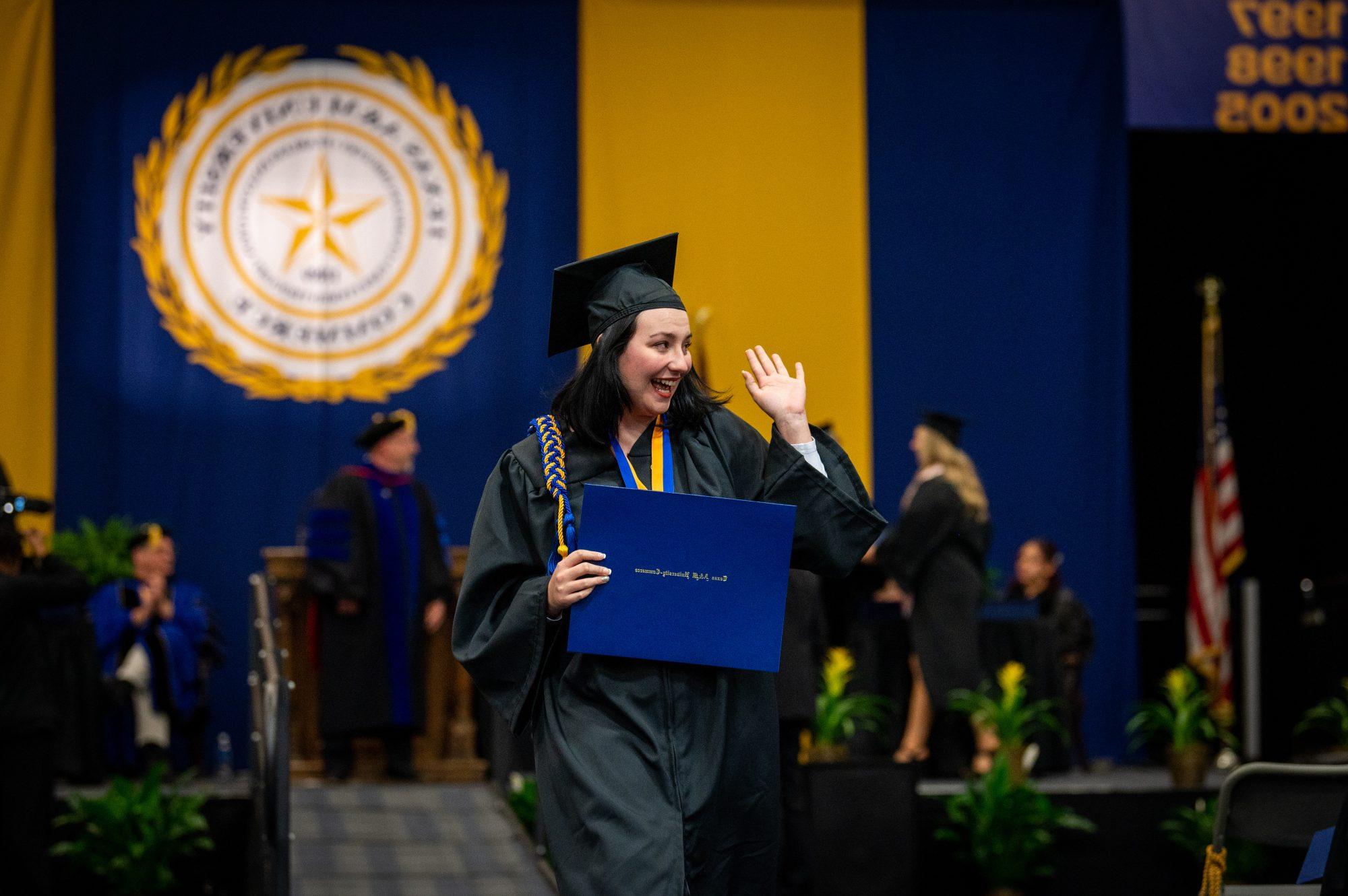 A female graduating student waging to the audience.