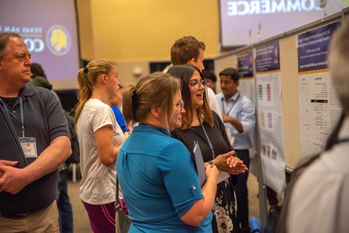 Several students and symposium attendees view research project posters.